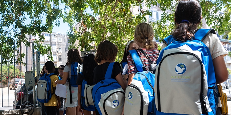 Children lining up for school wearing IFCJ backpacks