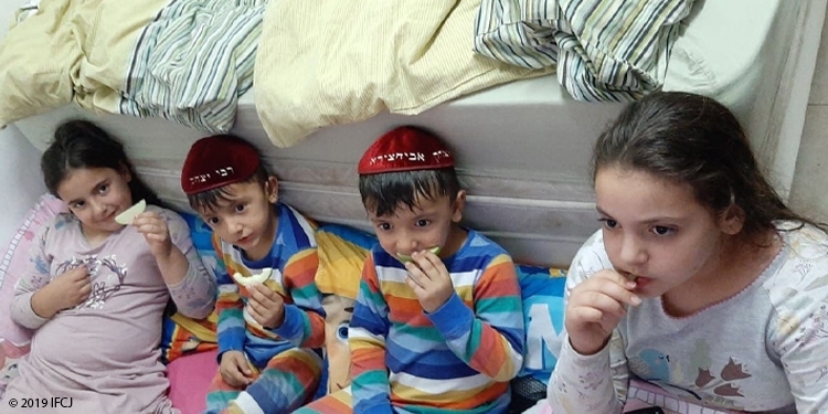 Four children sitting on the floor eating apples.