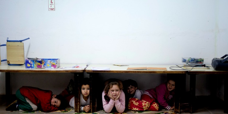 Five children taking cover under tables as alarms sound.