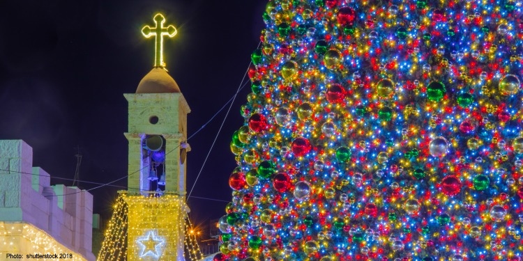 A lit-up Christmas tree full of ornaments next to a church.