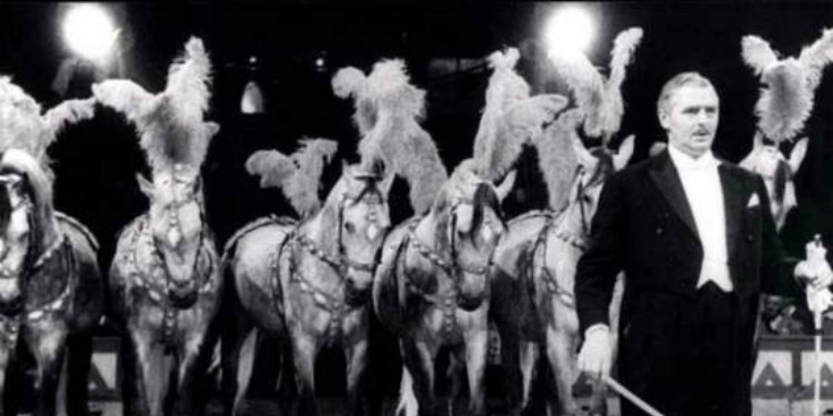 Man performing during a circus with horses behind him.