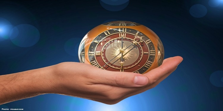 A hand holding a round clock against a blue background.