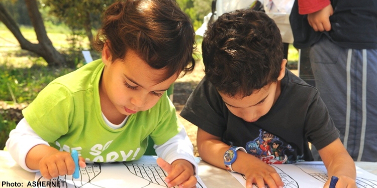 Two young boys coloring a page together with crayons.