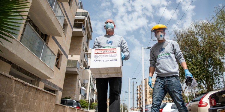 Two IFCJ staff members in masks walking with a food box.