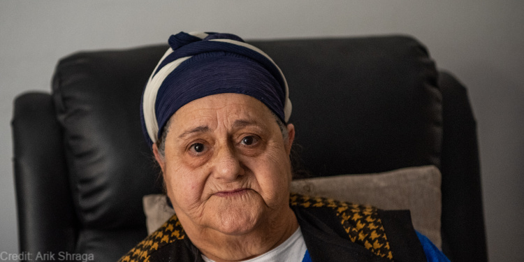 elderly woman, blue dress, black vest, blue and white headscarf