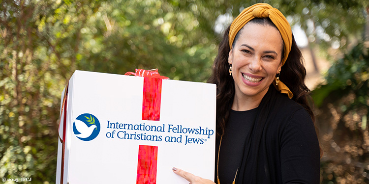 Yael Eckstein in a mustard headband holding an IFCJ food box with a ribbon on it.