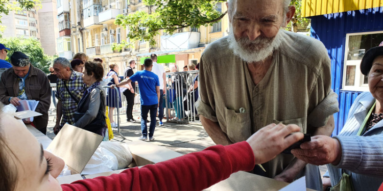 Elderly man smiling at woman passing out food boxes in Kyiv.