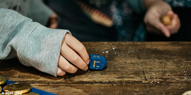 A person holding a dreidel on a wooden table.