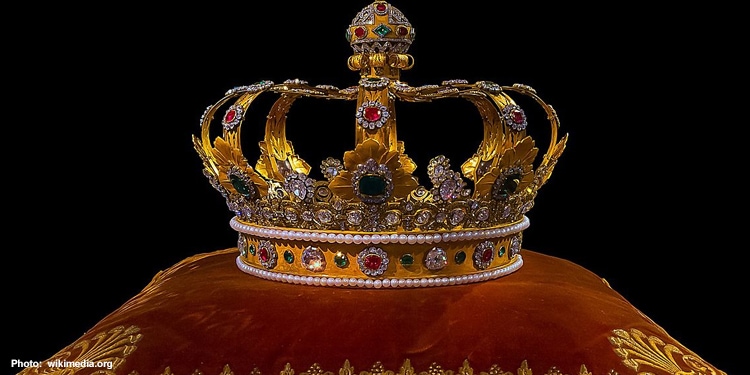 A bejeweled golden crown on an orange pillow.