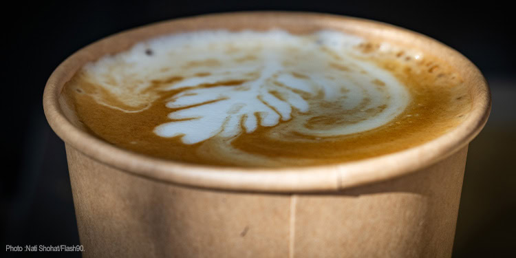 Close-up of a coffee cup featuring intricate latte art on the foam surface, served in a brown paper cup.