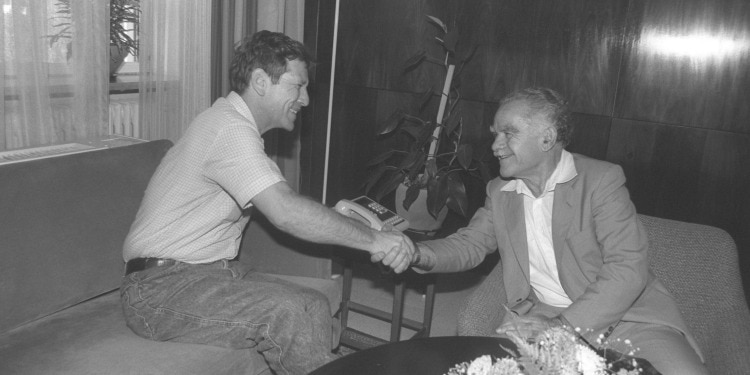 Black and white image of two men shaking hands while smiling at each other.