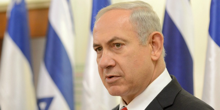 Bibi looking off in the distance with several Israeli flags behind him.