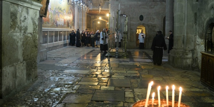 A tour group walking inside a temple with a candle with lit candles across the hallway.