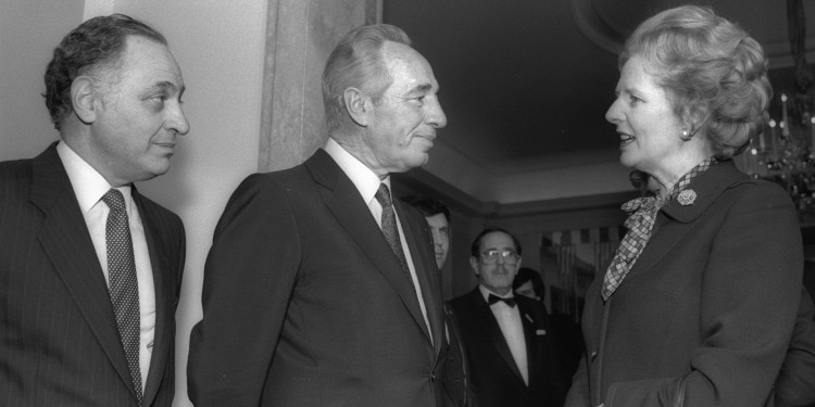 Two men in suits talking to a woman in formal attire.