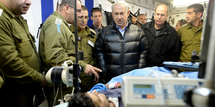 Bibi standing with several soldiers and medics while overlooking a wounded young man.