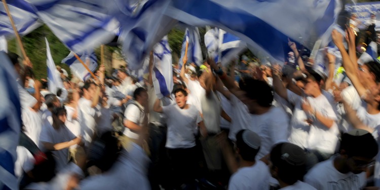 Several people gathering together while waving Israeli flags.