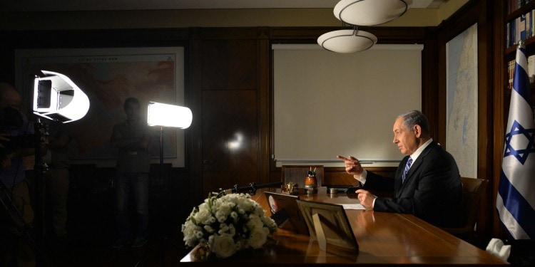 Bibi sitting at a desk while professional lights are shining on him while he's looking at a camera.