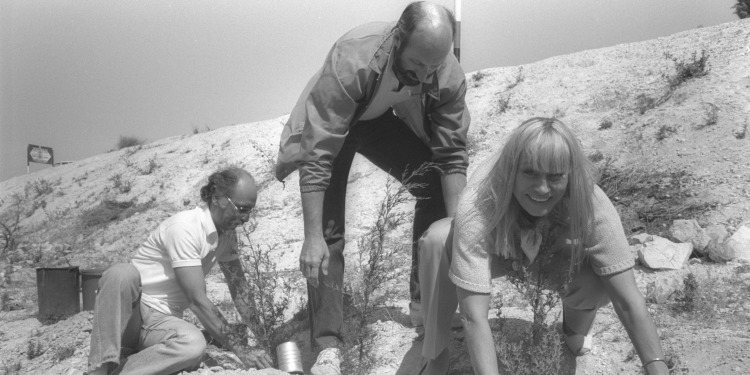 Black and white image of three people trekking a hill.