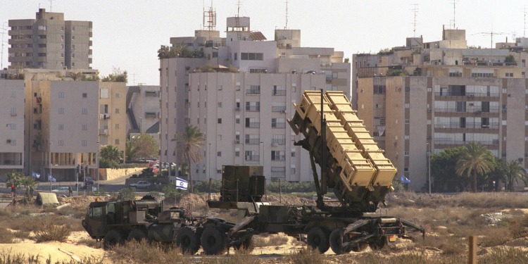 Large truck with cargo behind it outside of a city with concrete buildings.