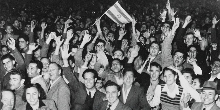 Group of young men and women waving their hands in the air with the Israeli flag.