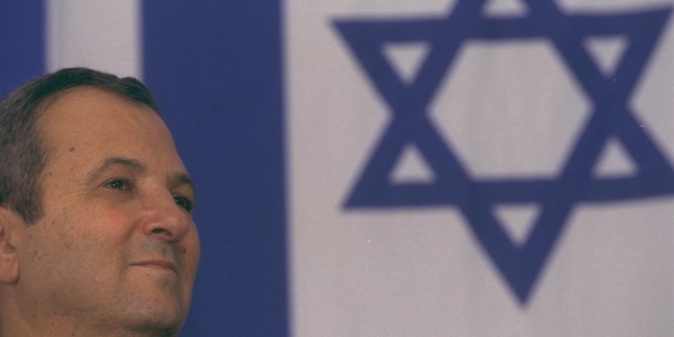 Man looking off into the distance with the Israeli flag behind him.