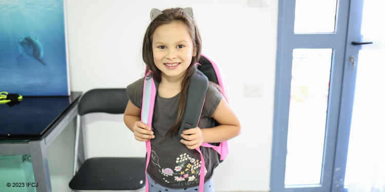 Young girl wearing a pink backpack.