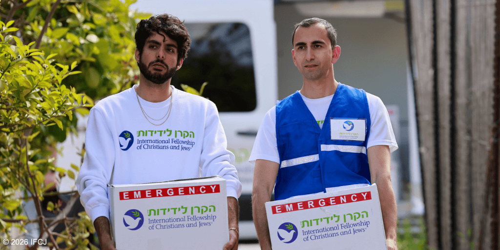 Two volunteers from IFCJ distributing emergency aid, holding a box with the IFCJ logo, in a community outreach effort.