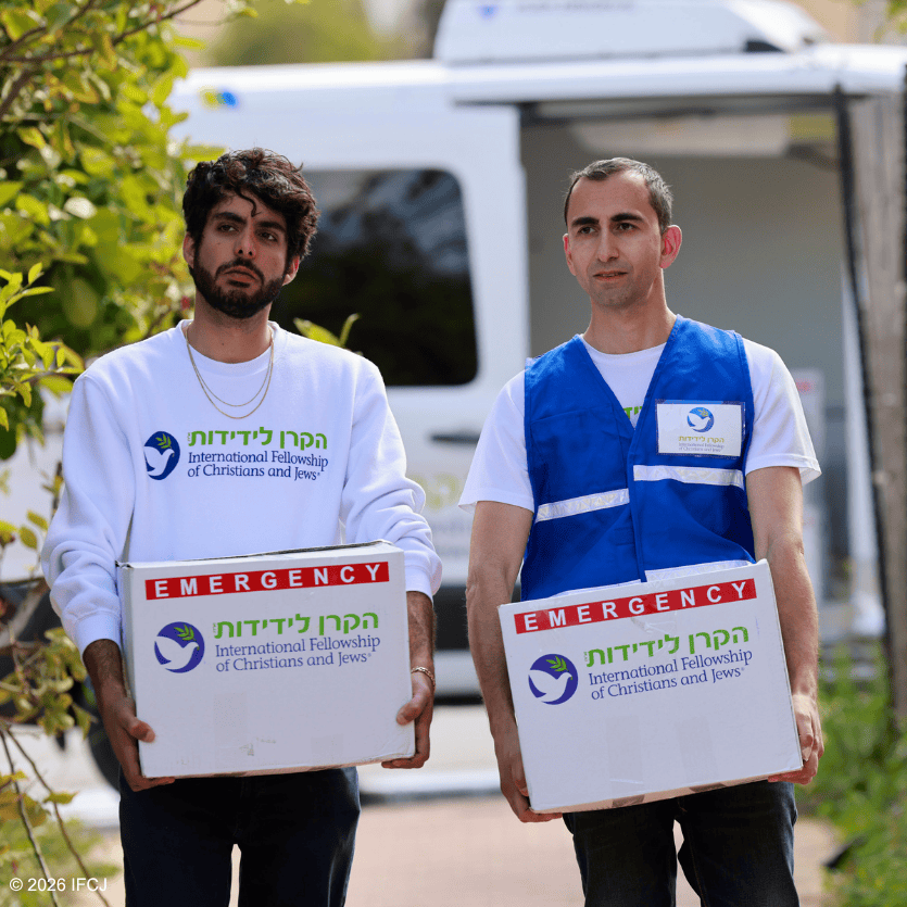 Two volunteers from IFCJ distributing emergency aid, holding a box with the IFCJ logo, in a community outreach effort.