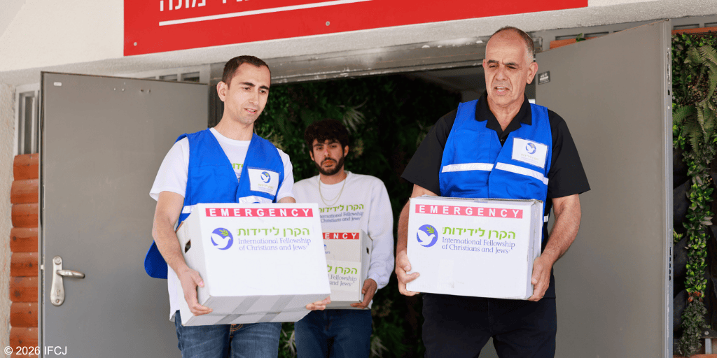 Three men in blue vests distributing boxes of emergency aid for IFCJ, supporting communities in need.