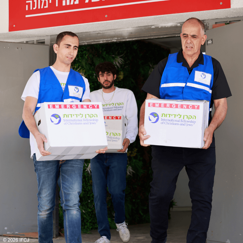 Three men in blue vests distributing boxes of emergency aid for IFCJ, supporting communities in need.
