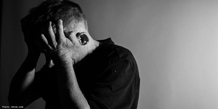 Black and white image of a man holding his head in his hands.