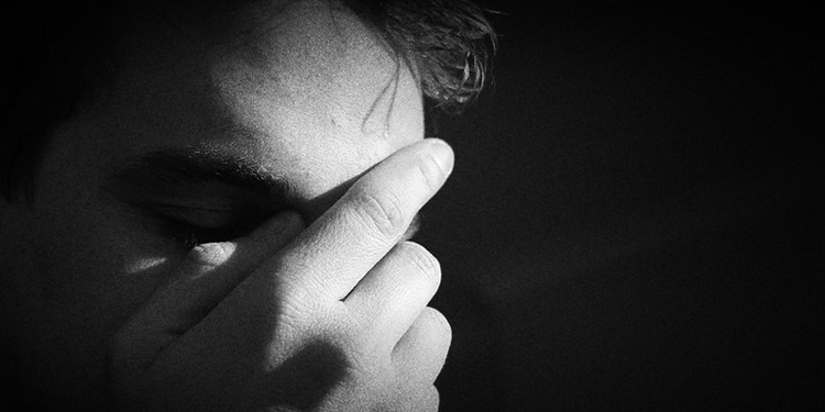 Black and white image of a man grabbing his brow while looking down.