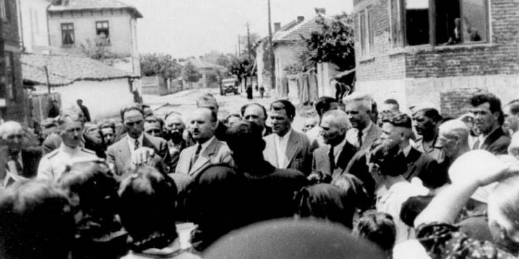 Black and white image of a man giving a speech in the street as people are crowded around him.