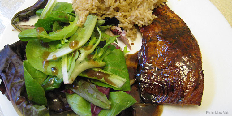 A dinner plate featuring a glazed fish fillet and a fresh green salad with mixed greens and vegetables.