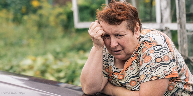 Elderly distraught woman leaning over with head propped up with her arm