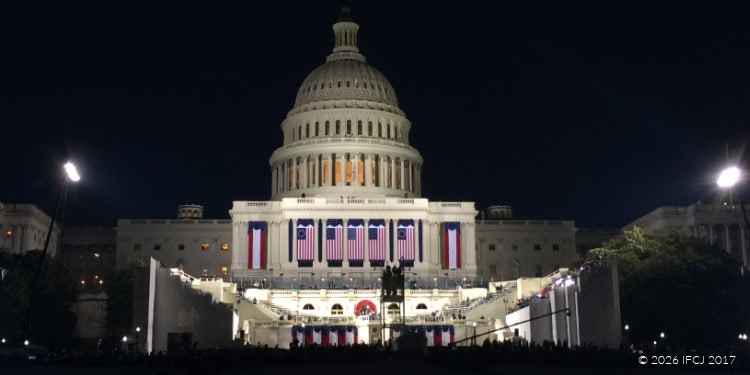 Night view of the U.S. Capitol building illuminated, with American flags displayed prominently, symbolizing patriotism and democracy.