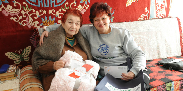 Two women sitting next to each other unwrapping an IFCJ given blanket.