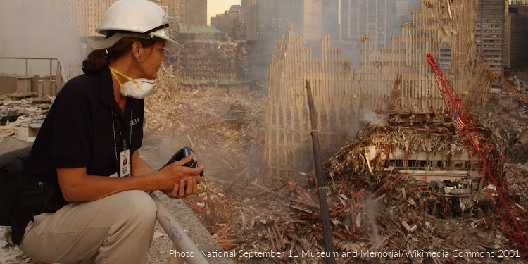 Rescue worker wearing a helmet and mask at Ground Zero, observing the destruction caused by the 9/11 attacks in New York City.