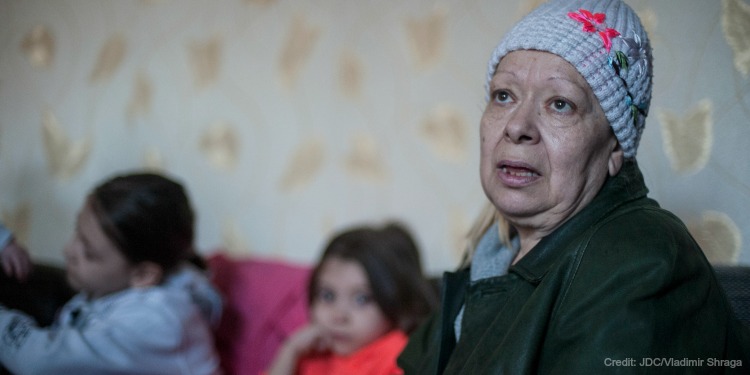 A middle aged Jewish woman in winter clothing inside her home with two young girls beside her.