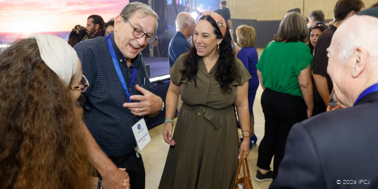 Group of diverse attendees at a conference, smiling and engaging in conversation, with a man wearing a badge and a woman in a brown dress center stage.
