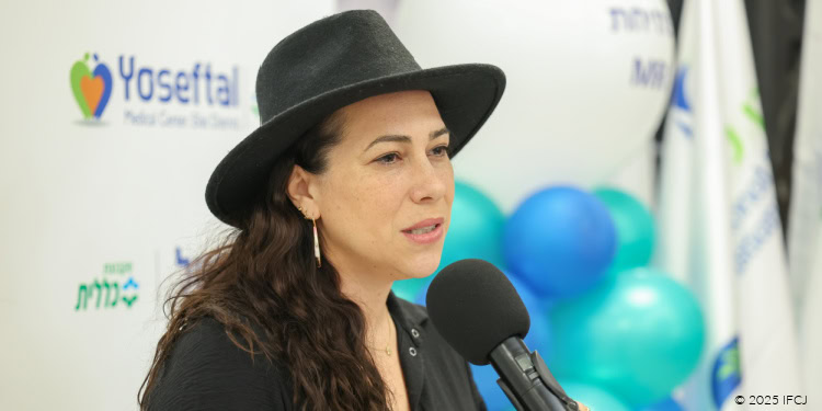 Yael Eckstein. black dress, black hat, microphone, podium