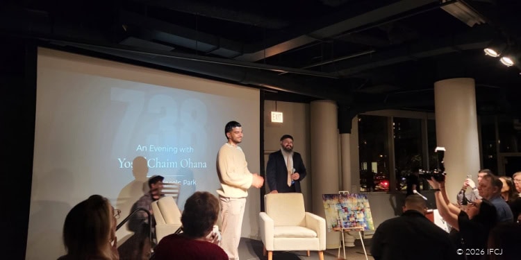 Group of people attending an IFCJ event, with a speaker on stage and audience members engaged in the presentation.