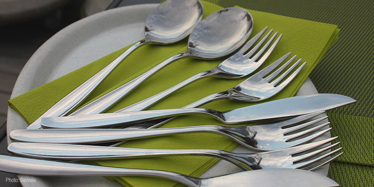 A set of polished silverware including forks, knives, and spoons arranged on a green napkin for a formal dining setting.