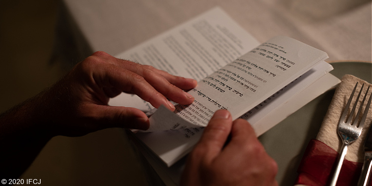 Hands holding book with Hebrew text.