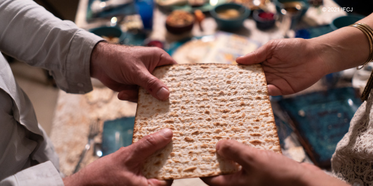 Two pairs of hands holding a single piece of matzah.