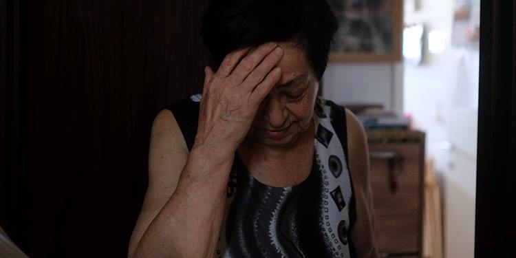 Elderly Jewish woman looking down at the floor while having her hand on her face.