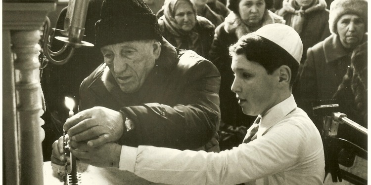 Black and white image of an elderly and teenage boy lighting a candle together.