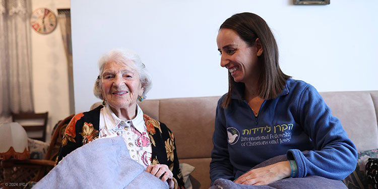 Elderly woman holding a blanket sitting with IFCJ staff