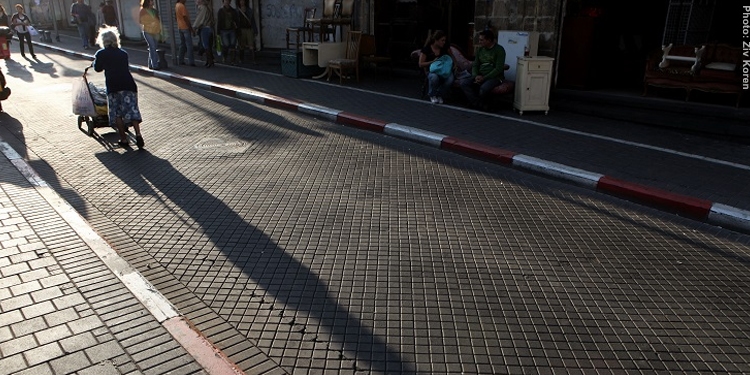 Elderly woman pushing a walker while walking down the street.