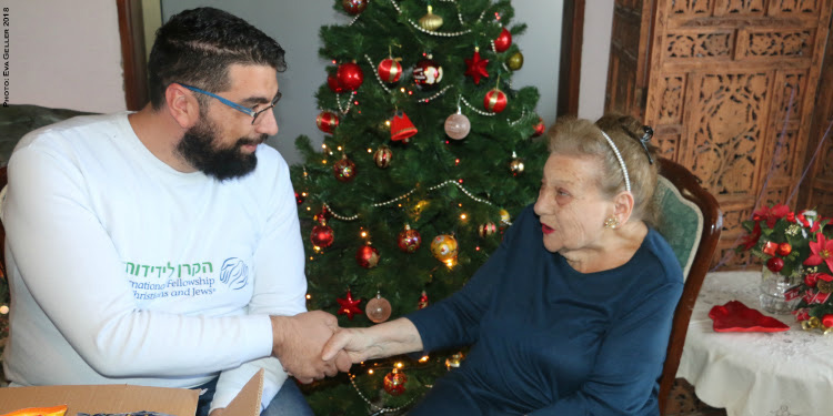 Elderly Jewish woman shaking hands with IFCJ volunteer.